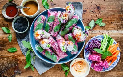 Färgglada vietnamesiska vårrullar med grönsaker och risnudlar, serverade med dippsåser och färska örter på en träbakgrund.
