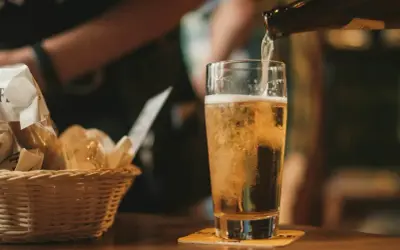 Złociste piwo IPA i APA leje się do szklanki. Obok koszyk z pieczywem.
