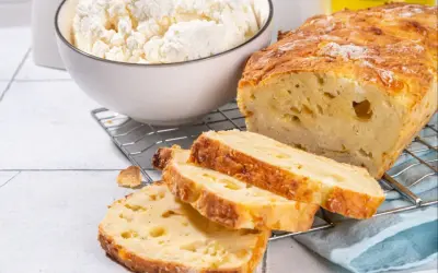 Wilgotny bochenek z twarogiem, pokrojony na kromki, obok miski z twarogiem.