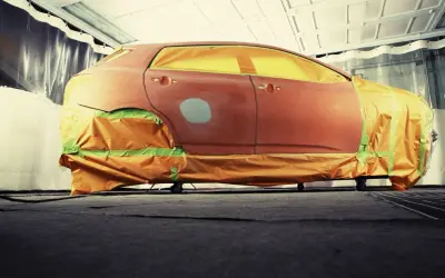 Auto in carrozzeria, pronta per verniciare con bomboletta. Finestrini e parti non interessate coperti con teli arancioni e nastro verde.