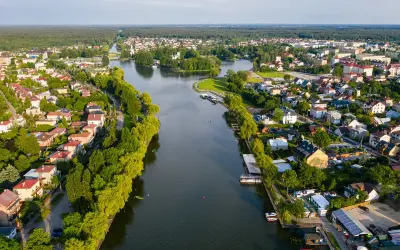 Malowniczy widok na Augustów i jego atrakcje: rzeka, zielone brzegi, domy i las w tle.