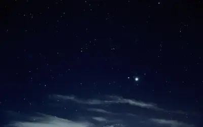 Nocne niebo pełne gwiazd, z widocznymi chmurami i dwoma jasnymi punktami, być może planetami.