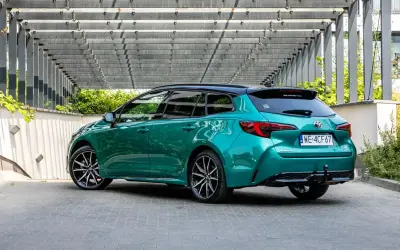 Zielona Toyota Corolla Hybrid kombi z czarnym dachem, zaparkowana pod nowoczesną pergolą.