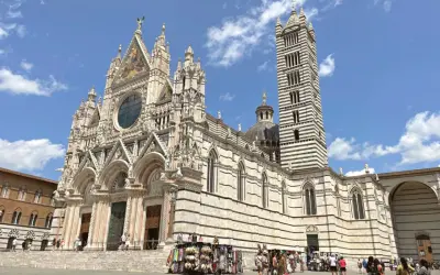 Il Duomo di Siena, con la sua imponente torre campanaria a strisce, è un must per chi cerca cosa visitare a Siena. La piazza antistante è animata da bancarelle.