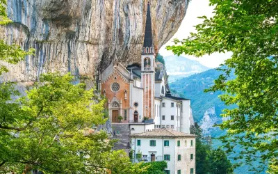 Suggestiva chiesa incastonata nella roccia, un gioiello architettonico vicino al Lago di Garda, circondata da verde lussureggiante e montagne.