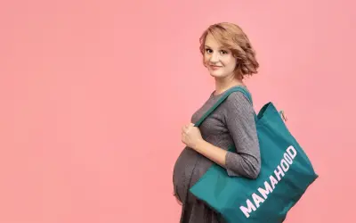 Przyszła mama z torbą "Mamahood" na ramieniu, gotowa do porodu.