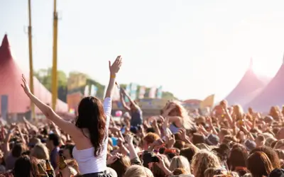Tłum ludzi na festiwalu muzycznym, z rękami w górze, w tle namioty i sceny.