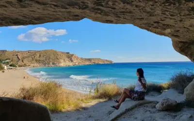 Mujer sentada en una cueva, contemplando la playa y el mar azul. Un lugar idílico que ver cerca de Cabo de Gata.