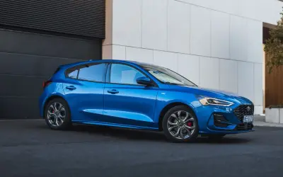 Błękitny hatchback Ford Focus stoi przed nowoczesnym budynkiem.