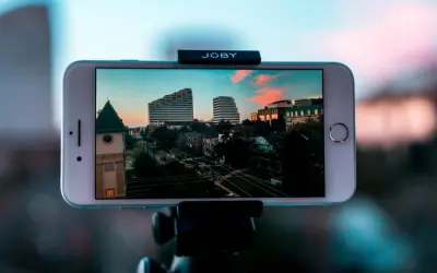 iPhone nagrywa timelapse miasta o zachodzie słońca. Widać budynki, drzewa i ulicę.
