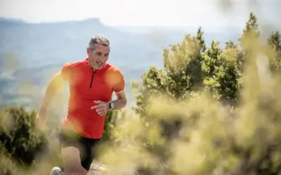 Un coureur trail en plein effort, souriant, sur un sentier de montagne ensoleillé.