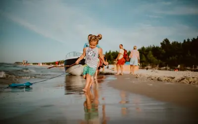 Dziewczynka z patykiem na plaży w Karwi. W tle łódź i ludzie, idealne karwia atrakcje dla dzieci.