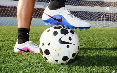 Un pied en crampons de foot, posé sur un ballon, sur l'herbe. Peut-on laver des chaussures de foot en machine ?
