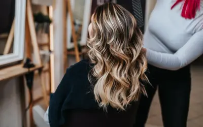 Frau mit wunderschöner blonde balayage Frisur, die im Friseursalon gestylt wird.