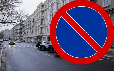 Znak B35 zakazu zatrzymywania się na mokrej ulicy z samochodami i kamienicami w tle.