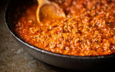 Herzhafte bolognese sauce köchelt in einer Pfanne, bereit für Pasta. Ein Holzlöffel rührt die fleischige Tomatensauce.