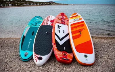 Cztery kolorowe deski SUP dla dzieci stoją na plaży, gotowe na wodne przygody.