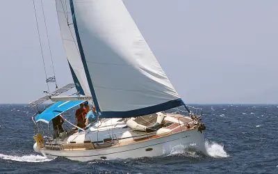 Un voilier blanc navigue sur une mer bleue agitée. L'équipage semble prendre un ris, ajustant les voiles pour mieux affronter le vent.