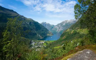 Widok na malownicze **Stavanger fiordy** z zielonymi zboczami gór, błękitną wodą i małym miasteczkiem u podnóża.