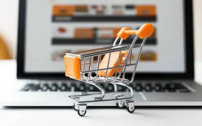 Miniaturowy wózek na zakupy przed ekranem laptopa symbolizuje najpopularniejsze sklepy internetowe i wygodne zakupy online.