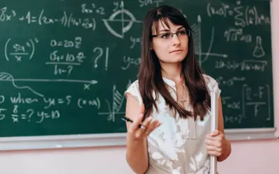 Nauczycielka matematyki w okularach, wyjaśniająca wzory na tablicy. Dofinansowanie do okularów dla nauczycieli to ważna sprawa.