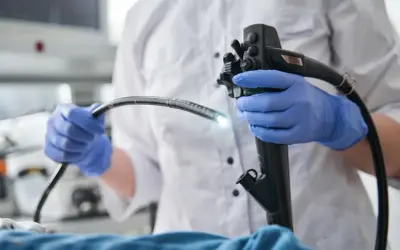 Lekarz w niebieskich rękawiczkach trzyma gastroskop. Badanie gastroskopia NFZ pozwala na diagnostykę.