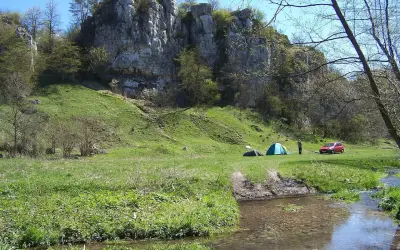 Malownicza dolina Kluczwody z rozbitymi namiotami, czerwonym samochodem i strumieniem.