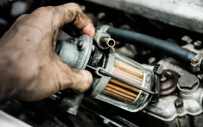 Brudna ręka mechanika wymienia zapchany filtr gazu. Objawy problemów z silnikiem mogą być różne, ale czysty filtr to podstawa.