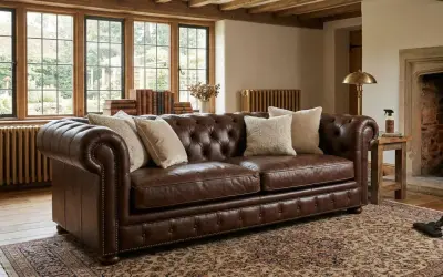 Brun Chesterfield-soffa i anilin skinn med knappad rygg och armstöd. Prydnadskuddar och en antik matta ger en varm känsla.