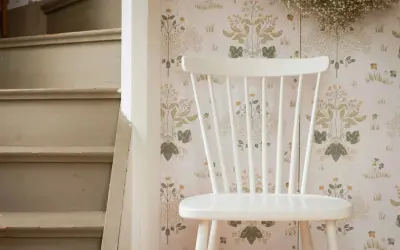 En vit stol står framför en blommig tapet. Bredvid syns en trappa som väntar på att måla om bord och stolar.