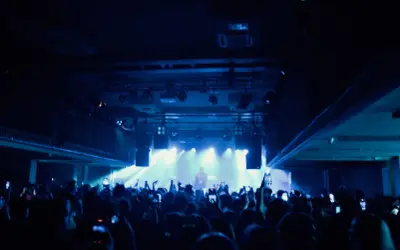 Tłum na koncercie lil tracy, ludzie nagrywają telefonami, światła sceniczne tworzą niebieską poświatę.