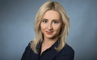 Portret uśmiechniętej blondynki w granatowej koszuli na niebieskim tle.