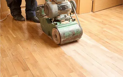Ein Handwerker bearbeitet mit einer Schleifmaschine einen Holzboden. Das Parkett wird abgeschliffen, um ihm neues Leben einzuhauchen.