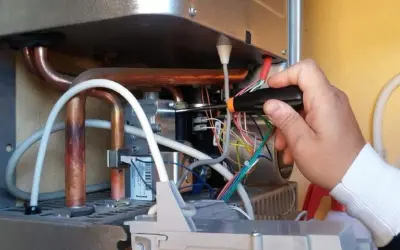 Tecnico effettua la pulizia della caldaia, lavorando sui cablaggi interni con un cacciavite.