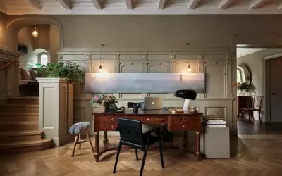Ett elegant skrivbord med laptop och lampa, i en hall med trappa och konst. Martin Brudnizki-inspirerad design.