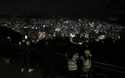 Nocny widok na rozświetlone miasto, przypominające panoramę Gangnam. Ludzie robią zdjęcia, podziwiając miejski krajobraz.