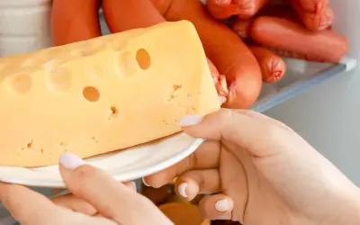Mano che prende un pezzo di formaggio svizzero dal frigorifero, tra altri tipi di formaggio e insaccati.
