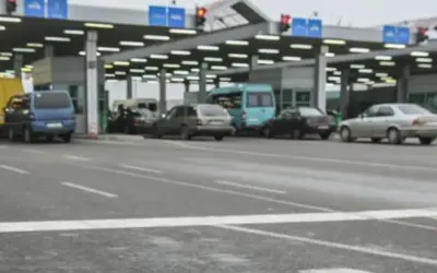 Kolejka samochodów na granicy polsko rosyjskiej. Widać budynki przejścia granicznego, sygnalizację świetlną i różne pojazdy.