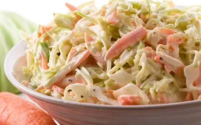 Miseczka surówki coleslaw z poszatkowanej kapusty i marchewki w kremowym sosie.