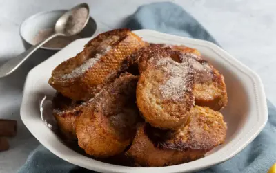 Un plato blanco lleno de torrijas españolas doradas y espolvoreadas con azúcar y canela.