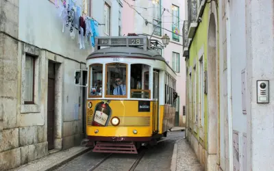 Gelbe straßenbahn lissabon fährt durch enge Gasse, Wäsche hängt über der Straße.