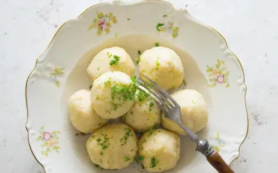 Pyszne pyzy wielkopolskie, delikatnie posypane natką pietruszki, czekają na widelcu na talerzu z kwiatowym wzorem.