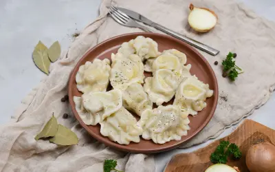Smażone pierogi z mięsem na brązowym talerzu, z cebulą i natką pietruszki w tle.