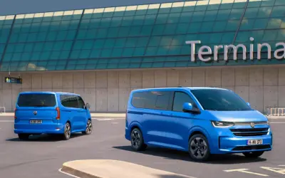 Dwa niebieskie Volkswageny Caravelle stoją przed budynkiem terminala lotniska.