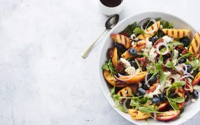 Salat mit Nektarinen, Blaubeeren, Ziegenkäse und Pekannüssen, garniert mit roten Zwiebelringen.