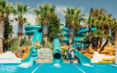 Vattenrutschkanor i Waterworld Ayia Napa med palmer och sol. Två personer åker i en ring nerför en blå vattenrutschkana.