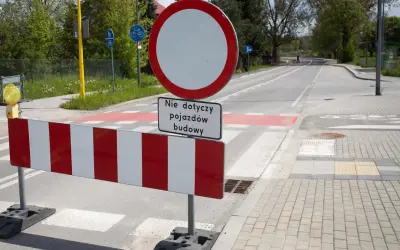 Znak B1 zakazu ruchu z tabliczką "Nie dotyczy pojazdów budowy" na tle drogi z pasami.