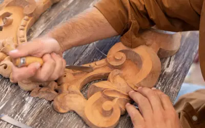 Un artisan utilise un ciseau pour sculpter le bois, créant des volutes complexes sur une pièce ornementale.