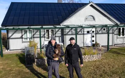 Två män och en hund framför ett hus med solpaneler på taket. Taket har vackra vinklar som ger huset karaktär.
