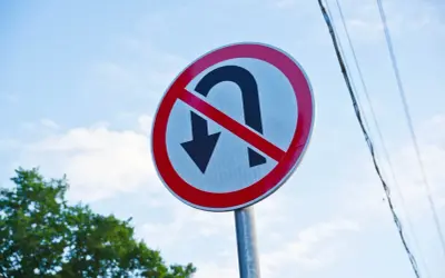 Znak zakazu zawracania na skrzyżowaniu. Nie można tu zawracać, więc lepiej jechać prosto lub skręcić.